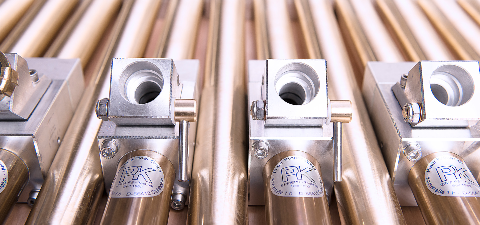 Metallische Präzisionskomponenten (Injektoren/Entlüftungsdüsen) der Peter Kröner GmbH, einem Spezialisten für Partikelschaumindustrie-Zubehör, mit sichtbarem 'PK'-Logo und modularem Design.