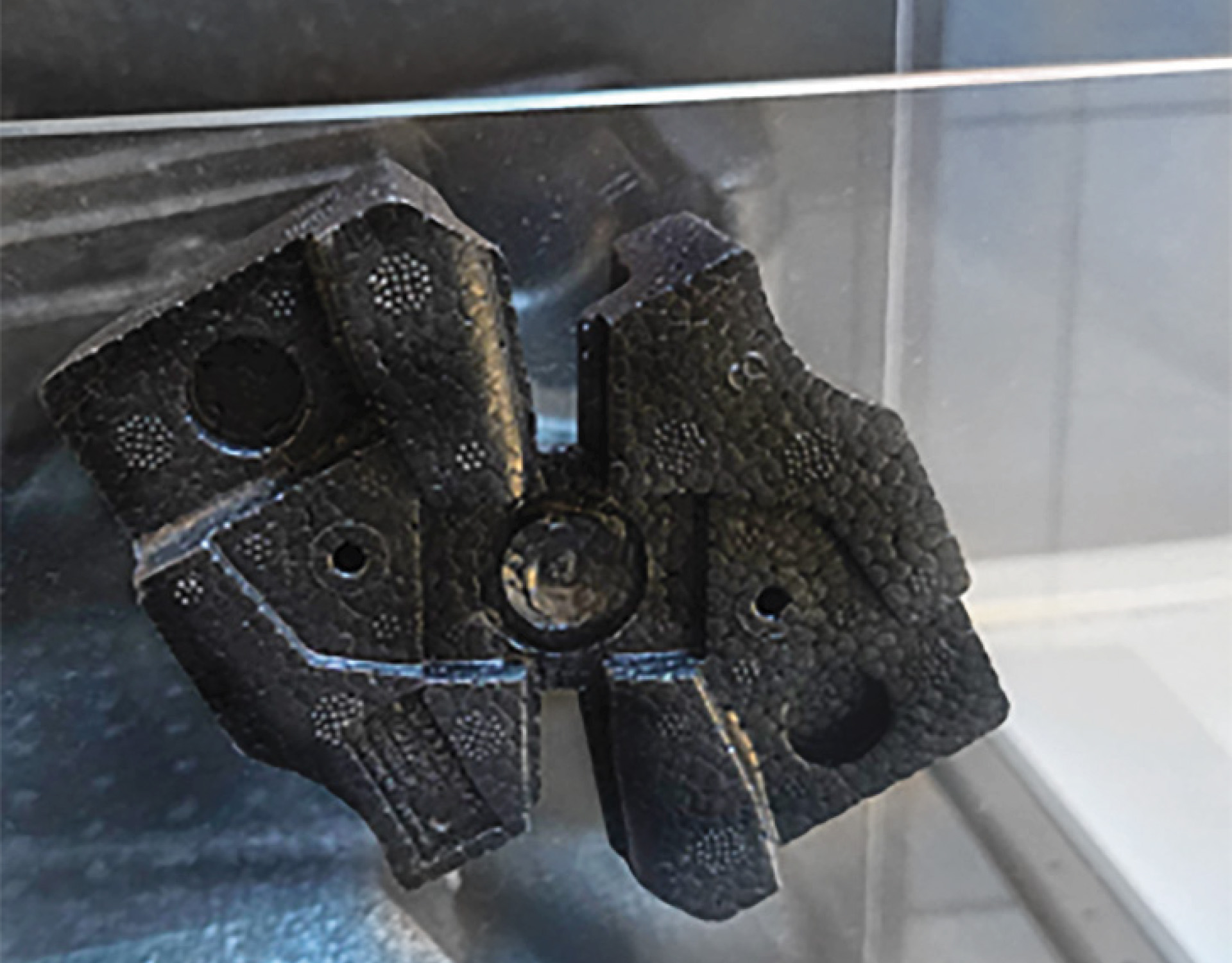 Dunkles, präzisionsgefertigtes Metallteil mit mehreren Löchern und einem zentralen runden Element, ein Beispiel für ein Teil zur industriellen Partikelschaumverarbeitung (z. B. Injektor oder Entlüftungsdüse).