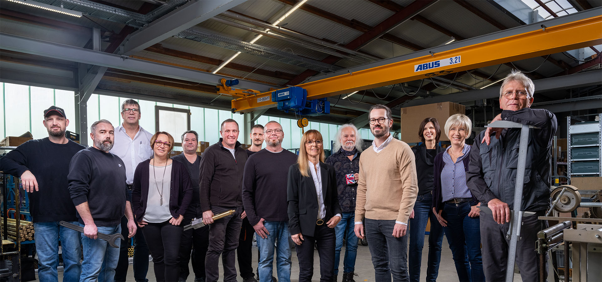 Gruppenfoto von Mitarbeitern der Peter Kröner GmbH in einer Werkstatt mit ABUS-Kran, darunter Fachkräfte für die Entwicklung und Fertigung von Injektoren und Zubehör für die Partikelschaumindustrie.