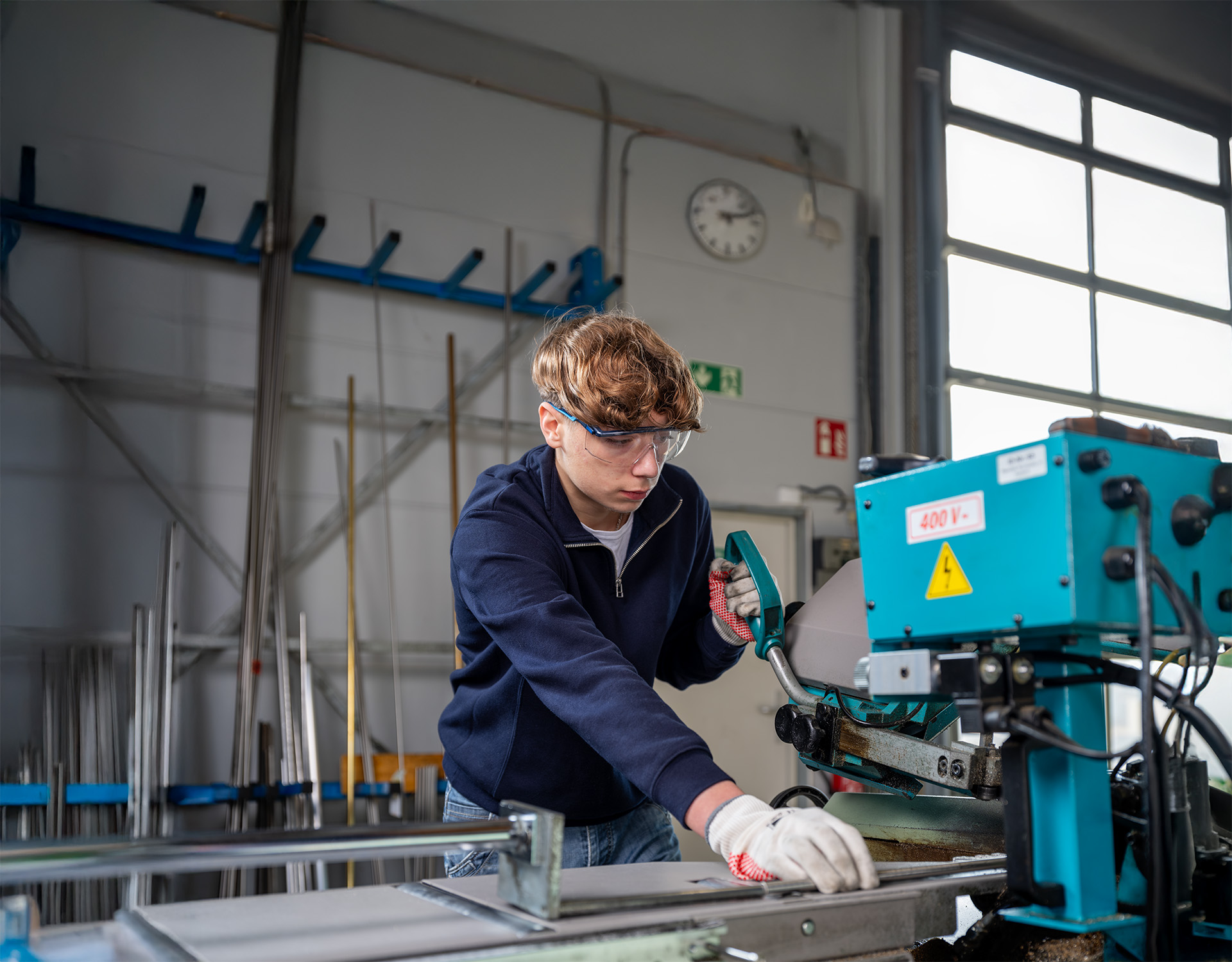 Ein Mitarbeiter bedient eine blaue 400V-Industriemaschine in einer Fertigungshalle, wo präzise Verarbeitung für die Partikelschaumindustrie im Mittelpunkt steht – wie bei Peter Kröner GmbH, das Injektoren, Entlüftungsdüsen und Zubehör für industrielle Anwendungen herstellt.