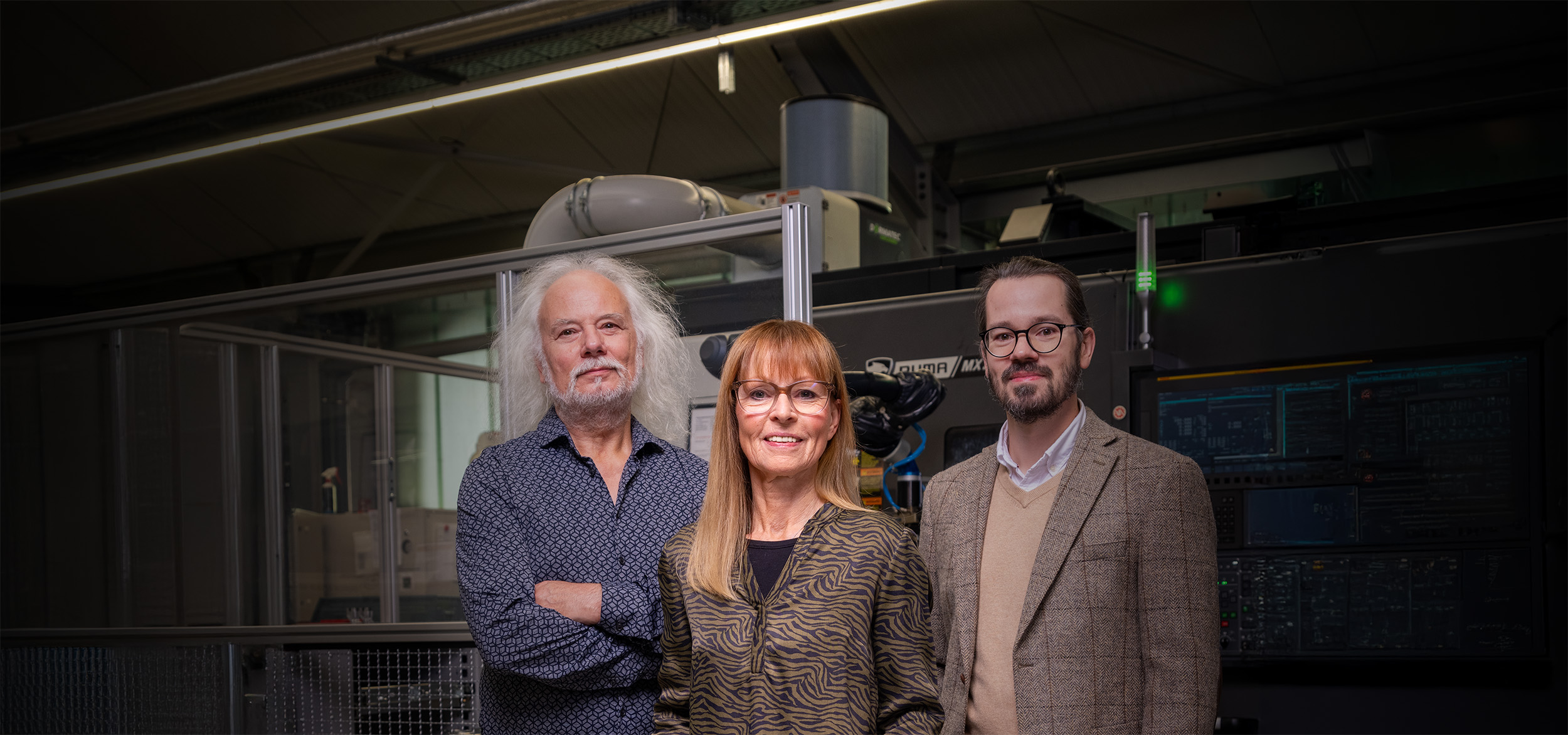 Drei Teammitglieder von Peter Kröner GmbH, einem familiengeführten Unternehmen, das Injektoren und Zubehör für die Partikelschaumindustrie entwickelt und fertigt, stehen vor industrieller Fertigungstechnik in der Werkstatt.